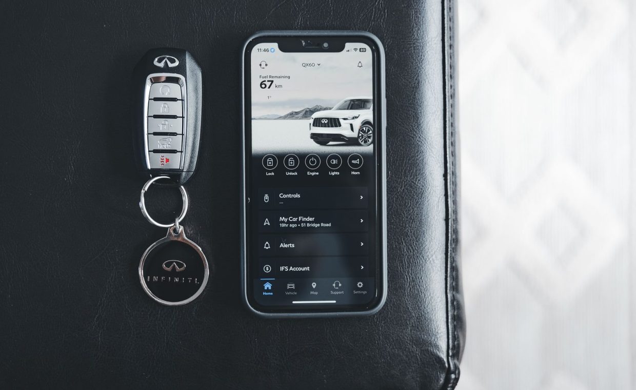 Close-up of an Infiniti key fob and smartphone displaying car app on a leather surface.