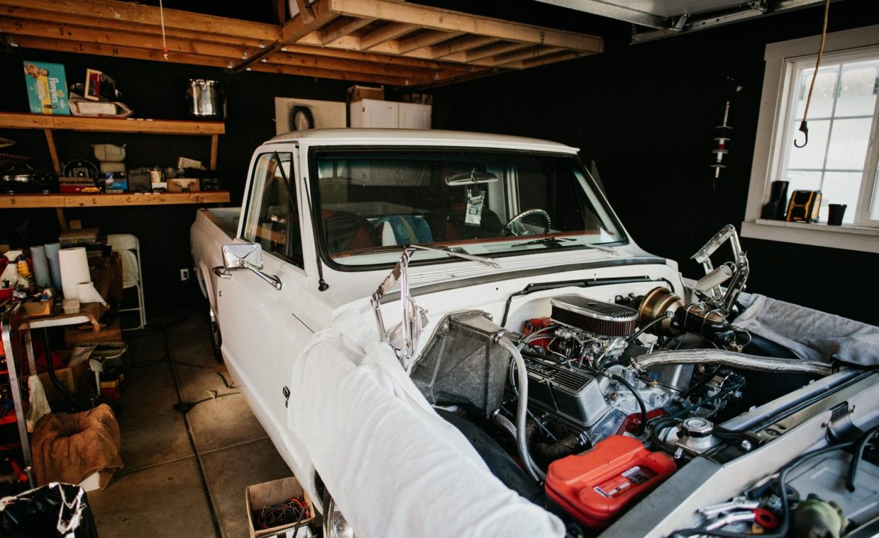 A vintage pickup truck undergoing engine repairs in a well-equipped home garage.