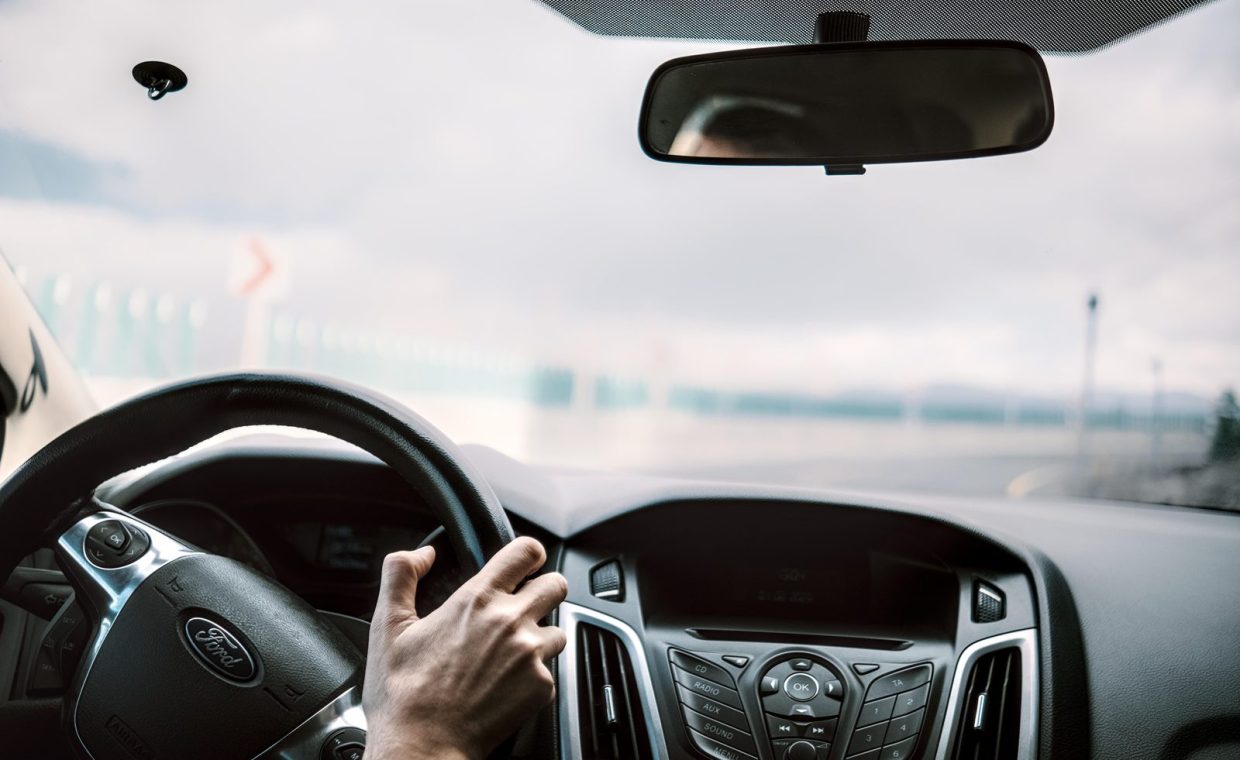 View from inside a car showing steering, rear-view mirror, and blurred road outside.