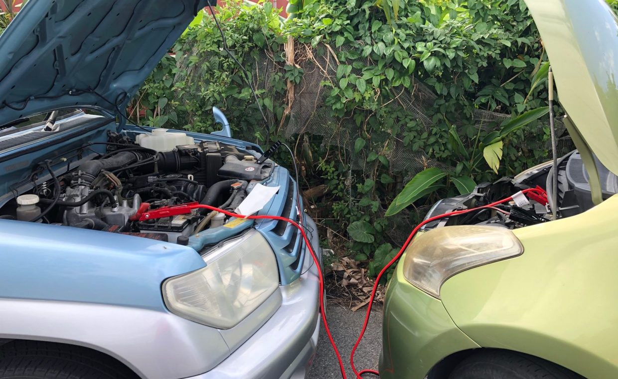 Two cars connected by jumper cables in a parking lot for a battery charge.