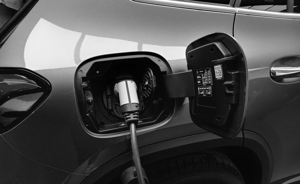 Close-up black and white image of an electric vehicle charging at a station.