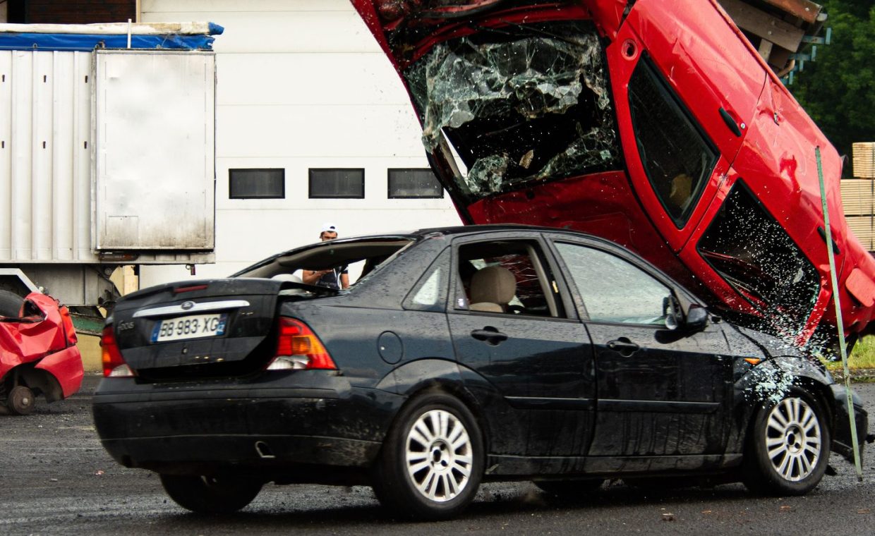 A thrilling car stunt crash with a red car flipped onto a black vehicle in an outdoor setting.
