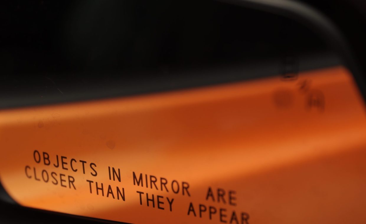 Detailed view of the warning text on a car side mirror, emphasizing road safety.