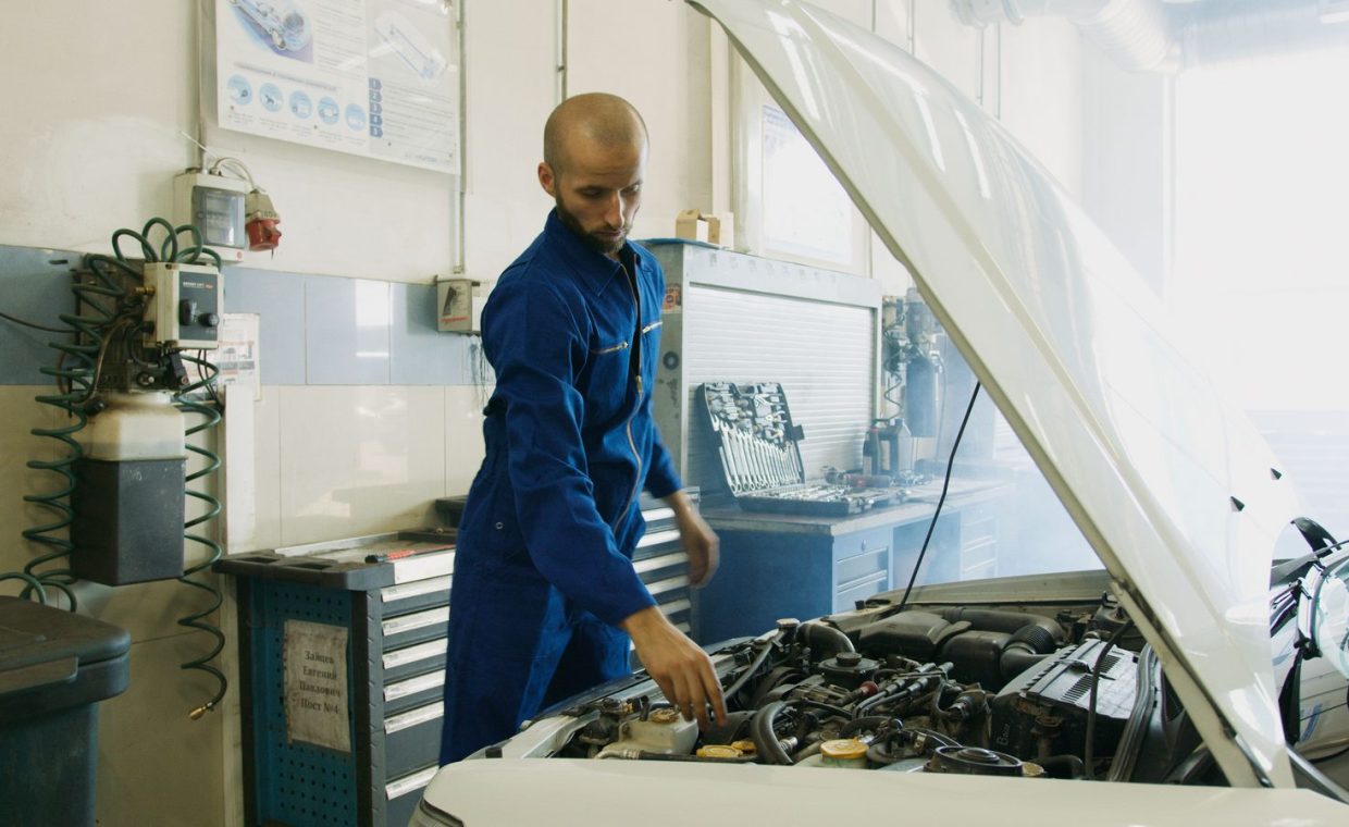Mechanic in blue uniform inspecting a car engine in a workshop.