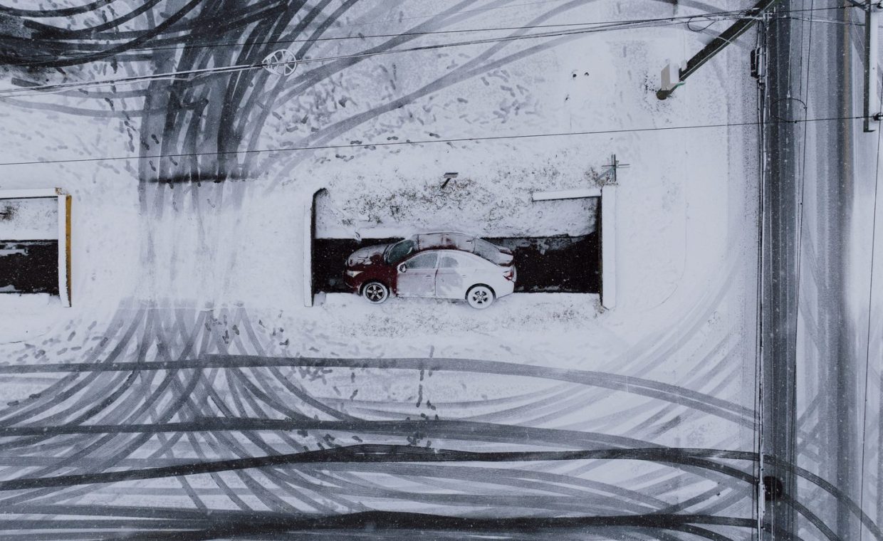 Aerial view of a red car in a snowy parking lot with tire tracks.