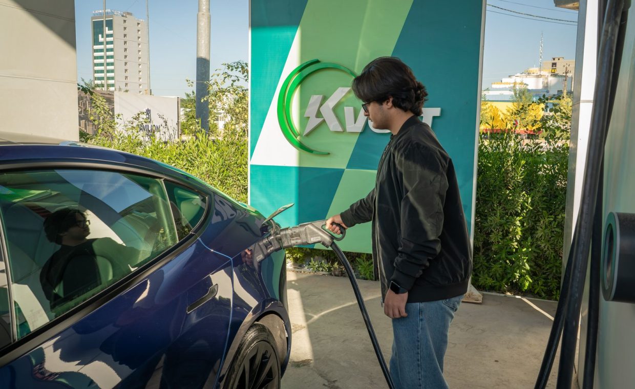 Young man charging a Tesla Model 3 at an outdoor electric vehicle station during the day.