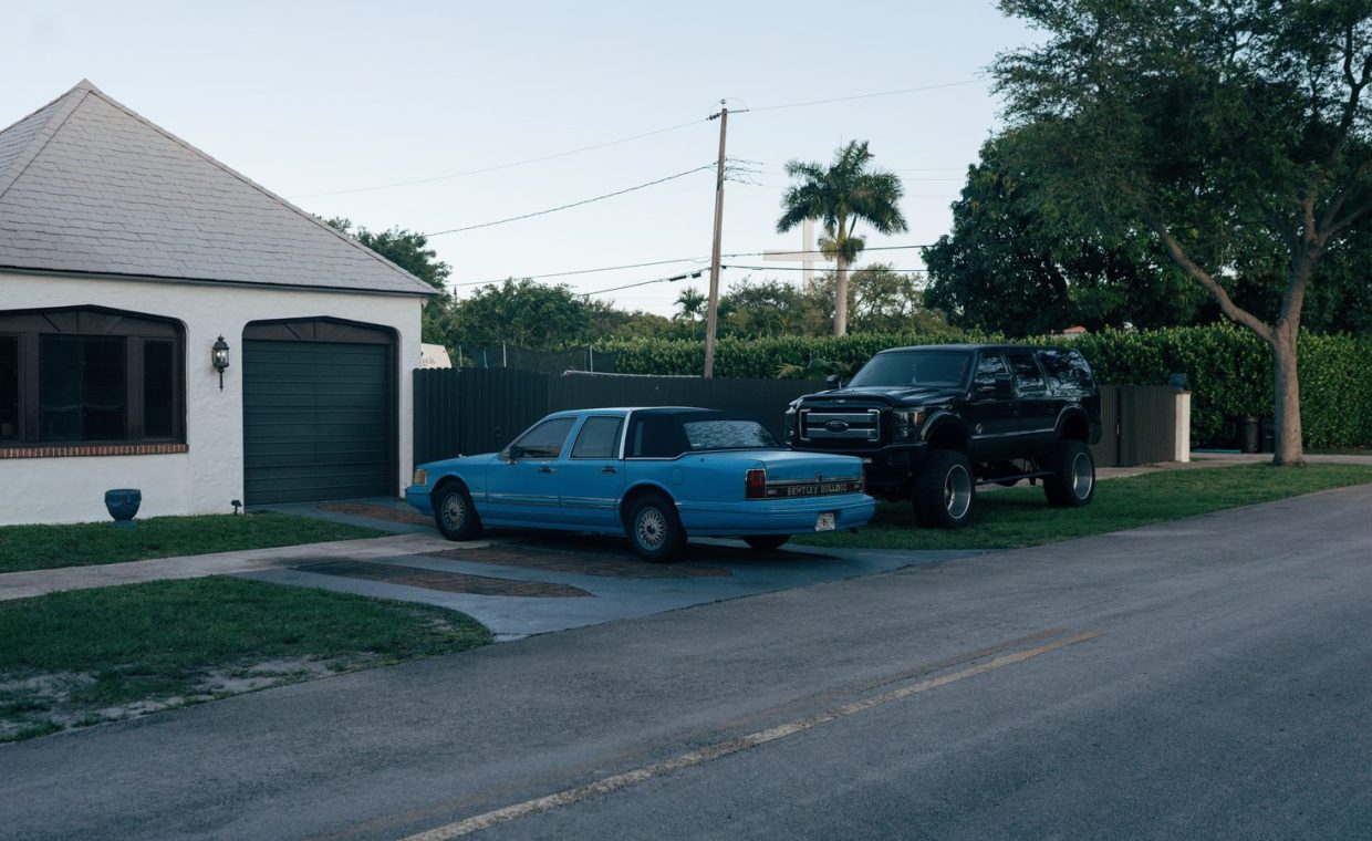 Classic and modern cars parked on a quiet residential street in a suburban neighborhood.