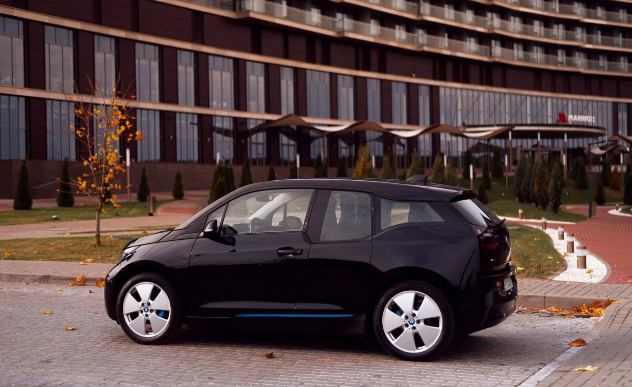 Black BMW i3 parked on city street with modern building backdrop, autumn.
